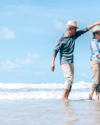 Two people in straw hats dancing in shallow ocean waves on a sunny beach
