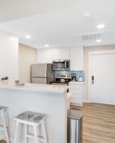 Modern kitchen with white cabinetry, stainless steel appliances, blue tile backsplash, island with seating, and wood flooring