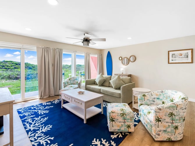 Open-plan living room with ocean view, wicker dining chairs, glass table, beige sofa, and coastal decor